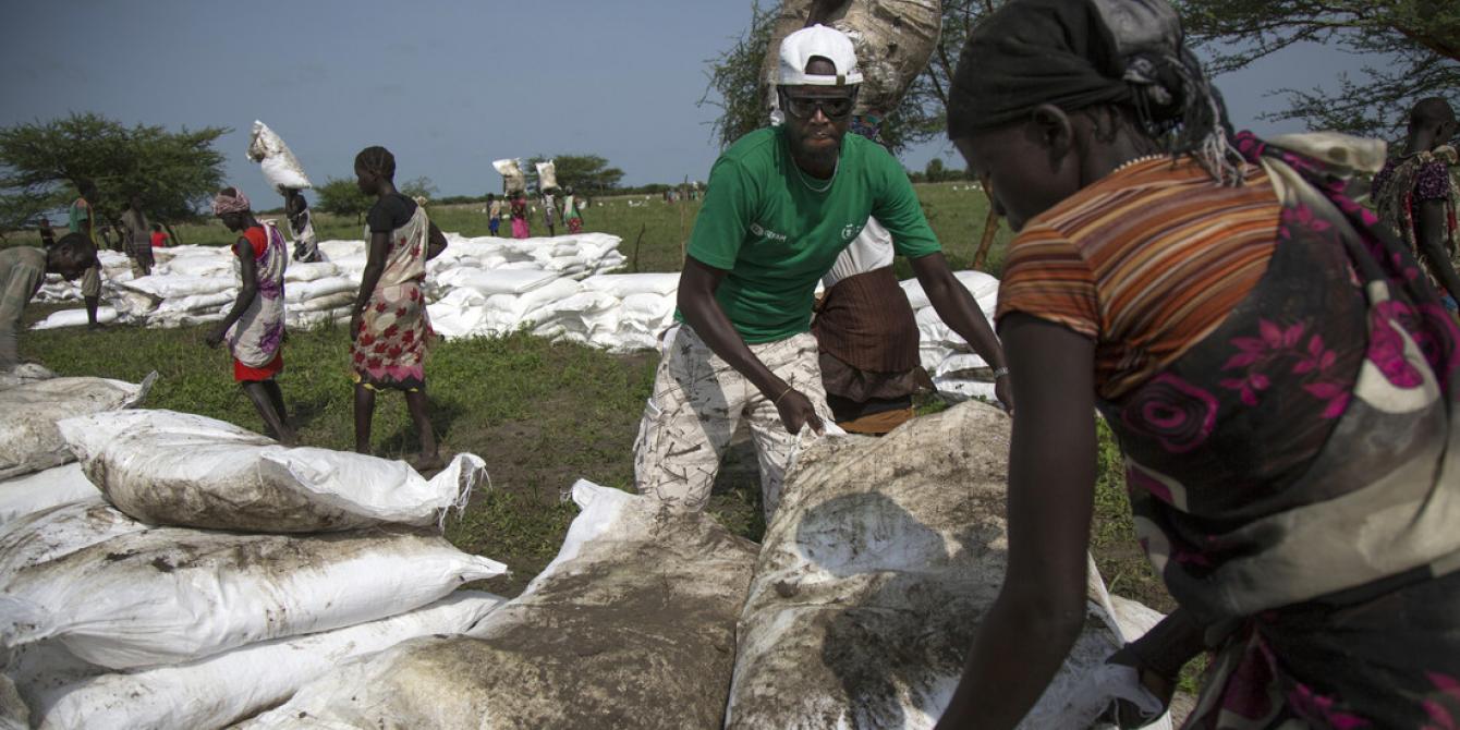 Oxfam staff helps a local staffer carrying sacks of food at a distribution in Pading, South Sudan. Albert González Farran/Oxfam