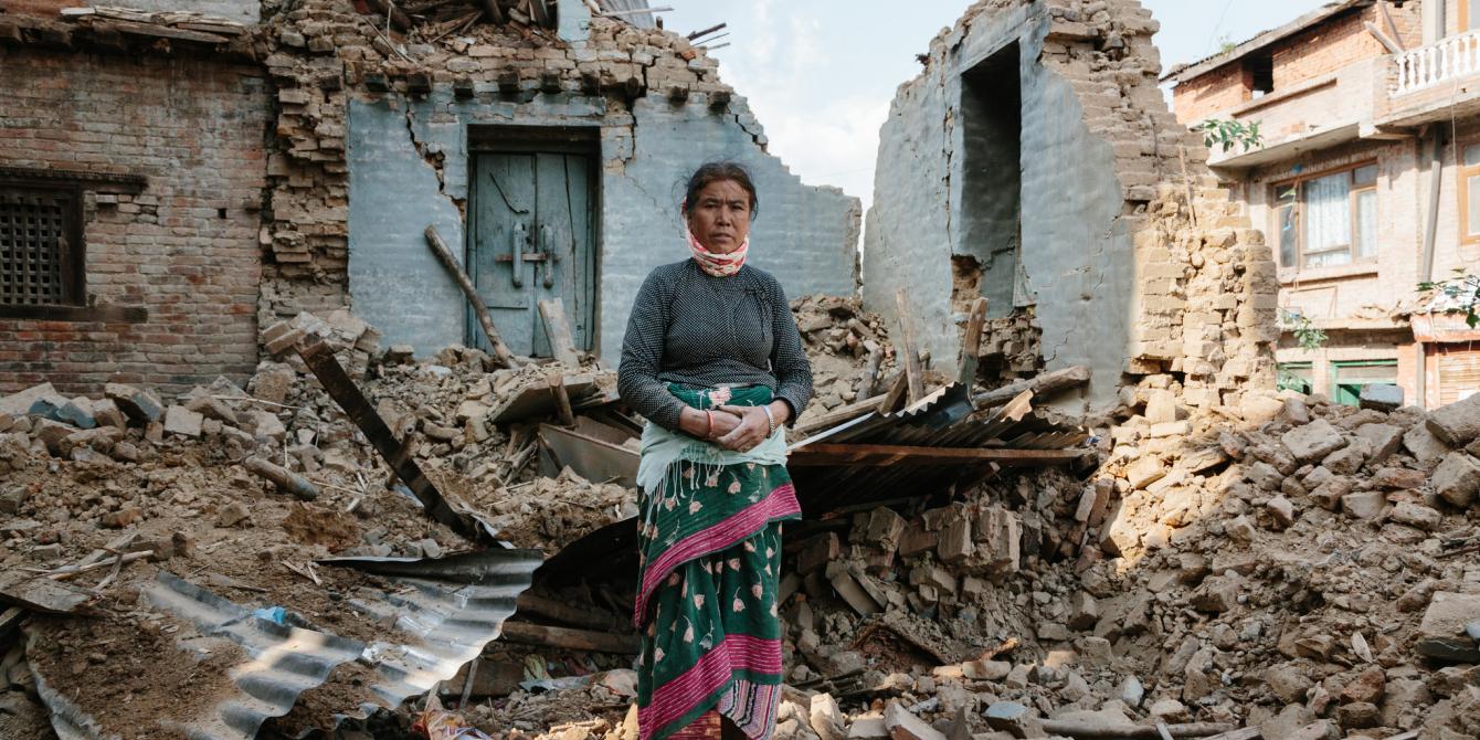 An earthquake survivors stands by her collapsed house - Credit: Aubrey Wade/Oxfam An earthquake survivors stands by her collapsed house - Credit: Aubrey Wade/Oxfam