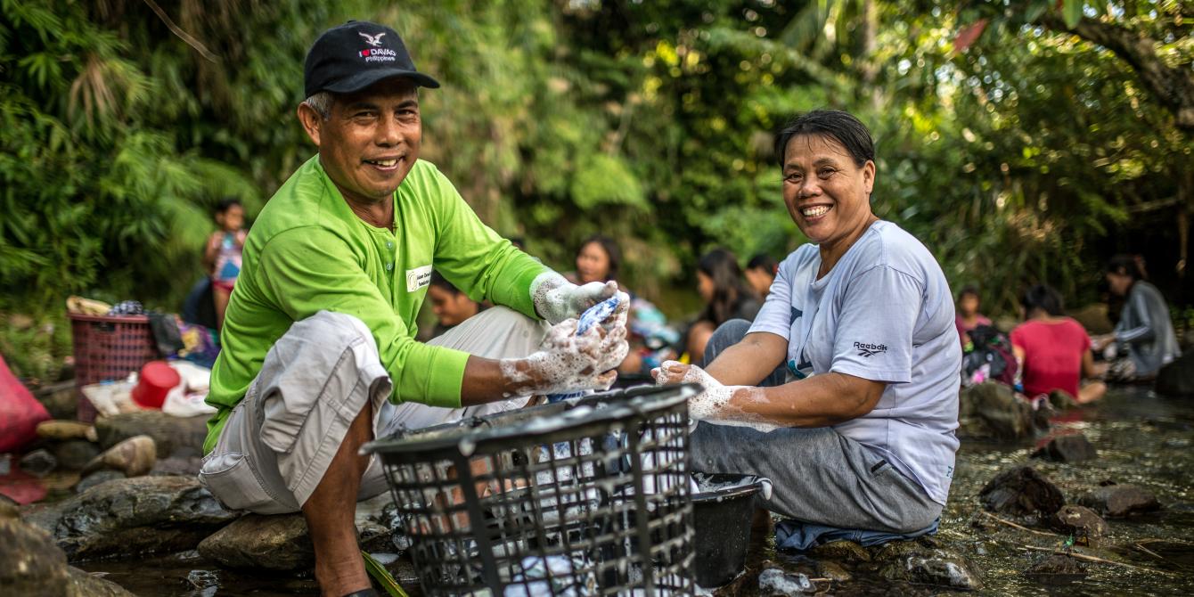 Husband and wife, Romulo and Pastora Samson, do laundry together at a local river and public laundry site in Barangay Santo Nino, Quinapondan, Eastern Samar. Access to water is a challenge in the fishing community. The river is their main source of water and requires several trips for water collection and laundry. Romulo and Pastora share laundry and household tasks, especially when Romulo is not fishing out at sea. (Photo: Aurelie Marrier d’Unienville/Oxfam)