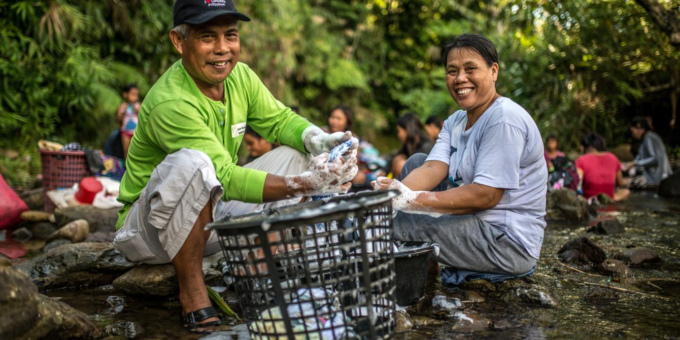 Spouses Romulo and Pastora Samson share care responsibilities at a local river and public laundry site in Barangay Santo Nino, Quinapondan, Eastern Samar. Access to clean water is a challenge for their community of farmers and fisherfolk because they need to take several trips to the river to bathe, collect water for the household, or wash their clothes. Now, with their local government recently enacting an ordinance on unpaid care work, their barangay must provide them with easier access to a safer water s