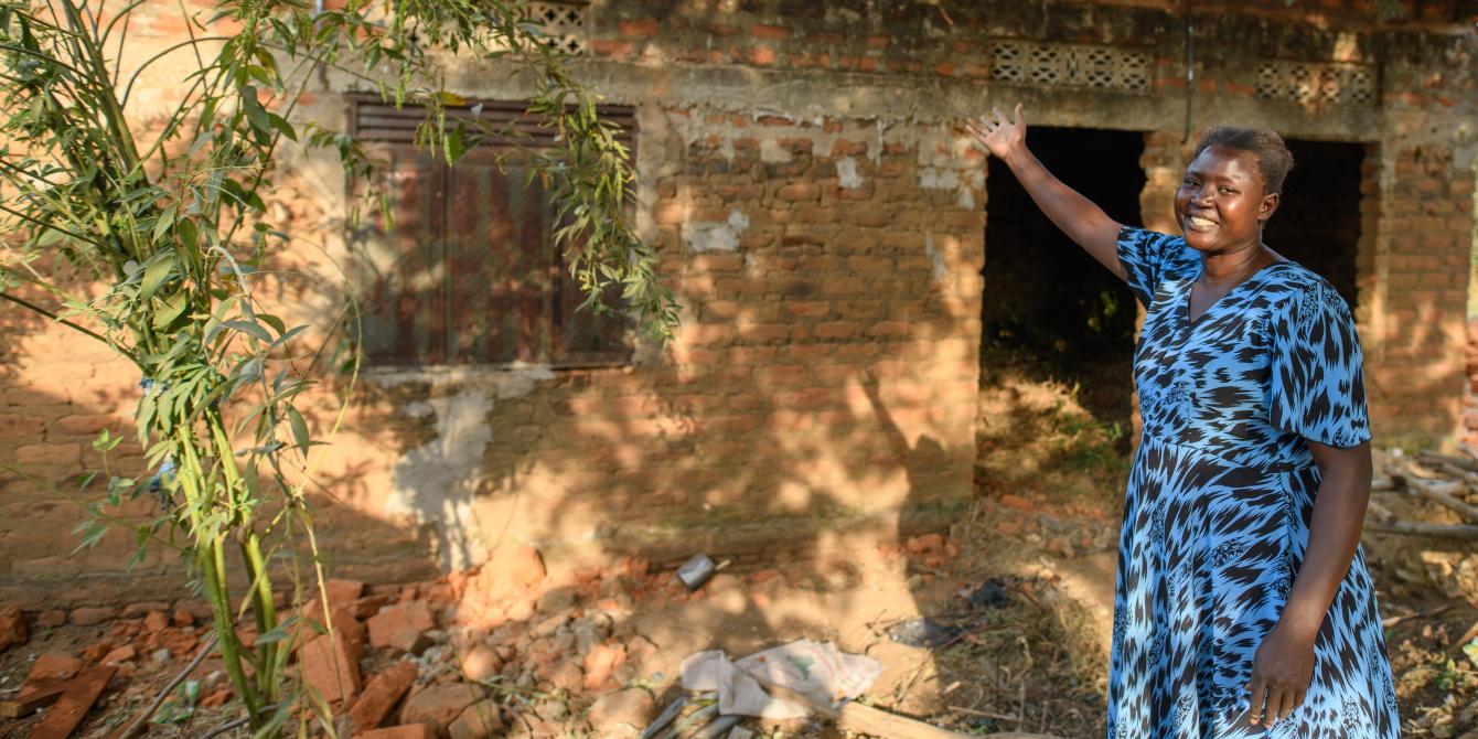 Badaru Lilian pointing at her house she is constructing from her savings. Through the youth economic empowerment project, Oxfam supported youth with business and entreprenuership skills. Youth like Lilian were able to start small businesses and save. Photo credit: Oxfam