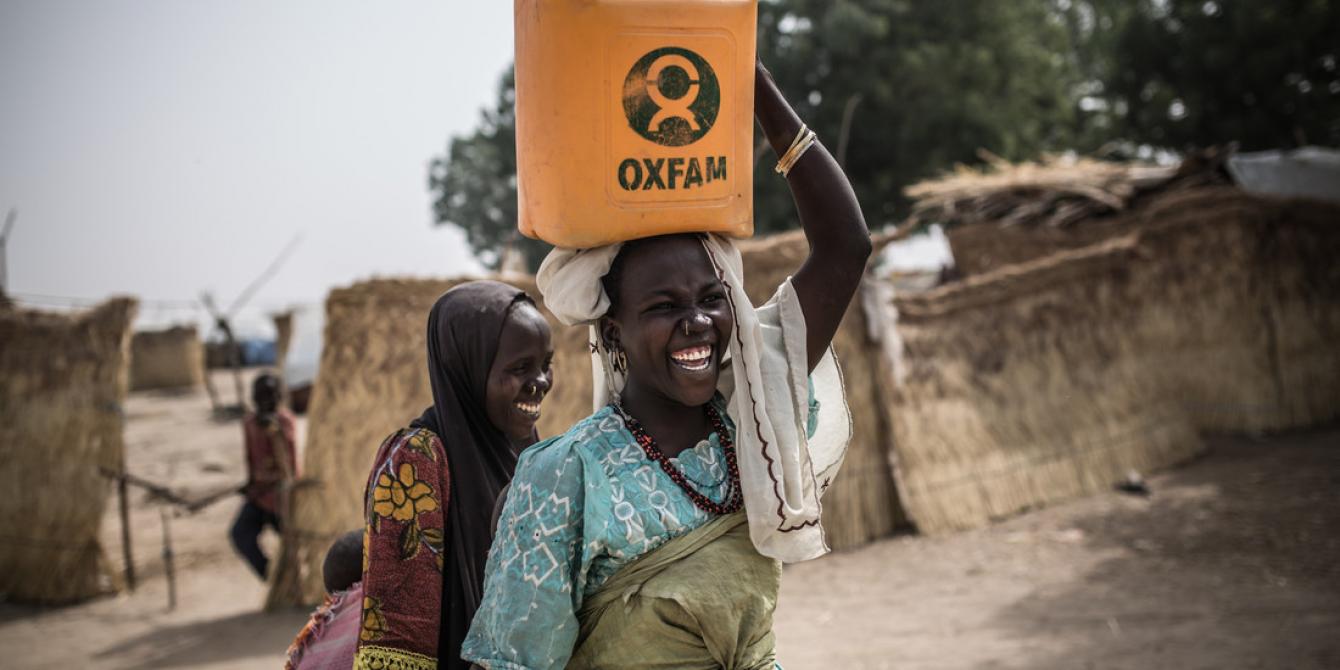 Deux femmes portent de l'eau dans des jerricans Oxfam à Muna Garage, un camp de personnes déplacées situé au Nigéria. Crédit: Pablo Tosco / Oxfam